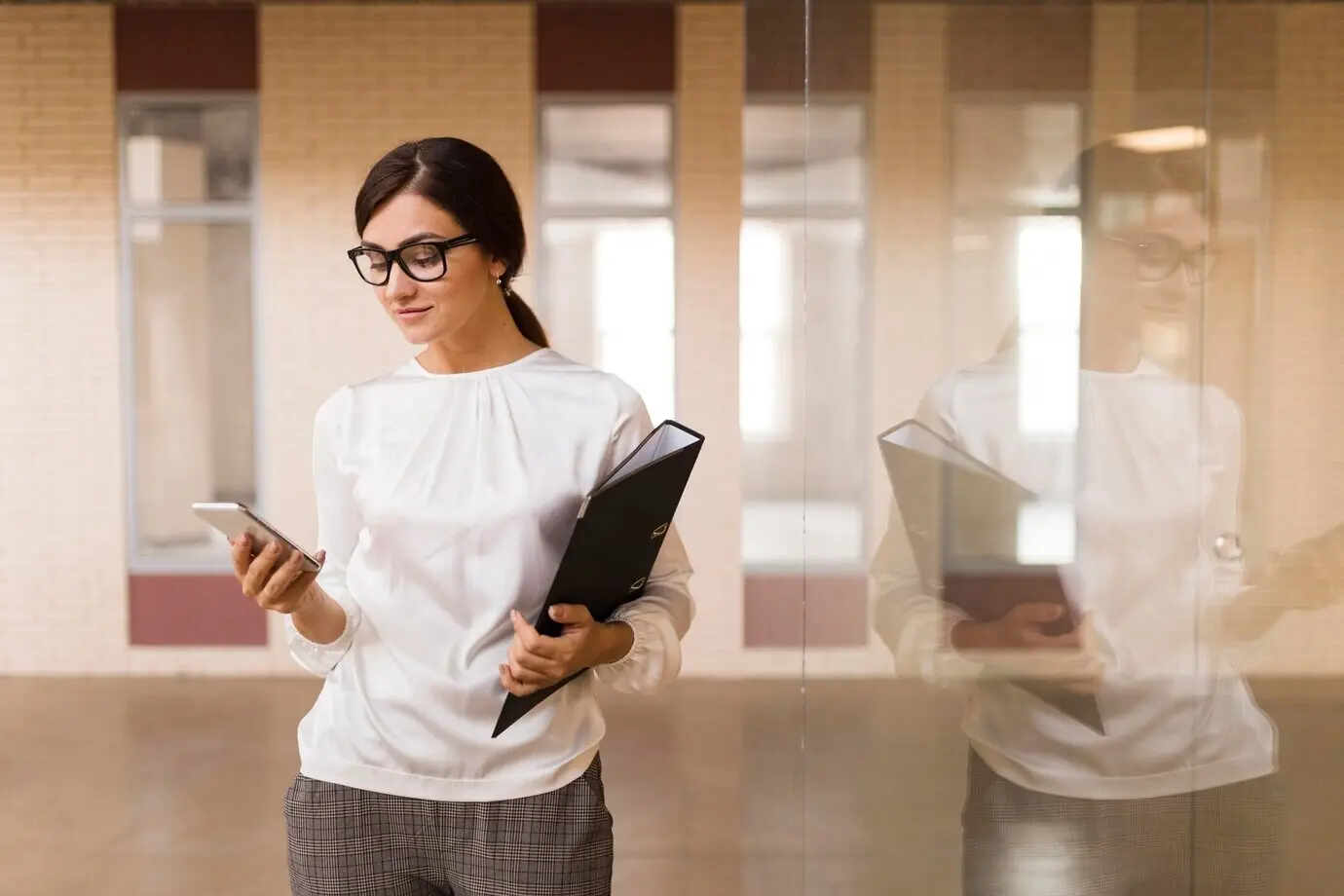 Front-facing view of a businesswoman with a smartphone and a binder in the office.